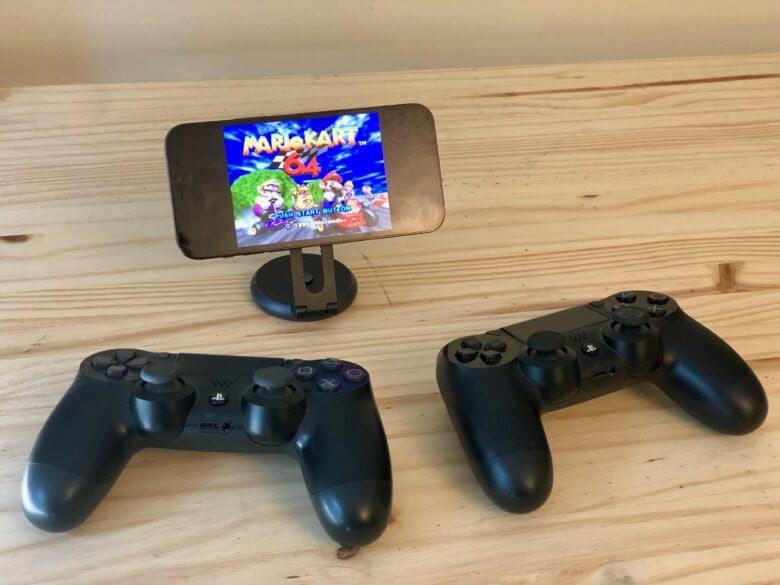 iPhone auf SwitchEasy-Ständer mit zwei PS4-Controllern, die Mario Kart 64 auf dem Delta-Spielemulator für iPhone spielen